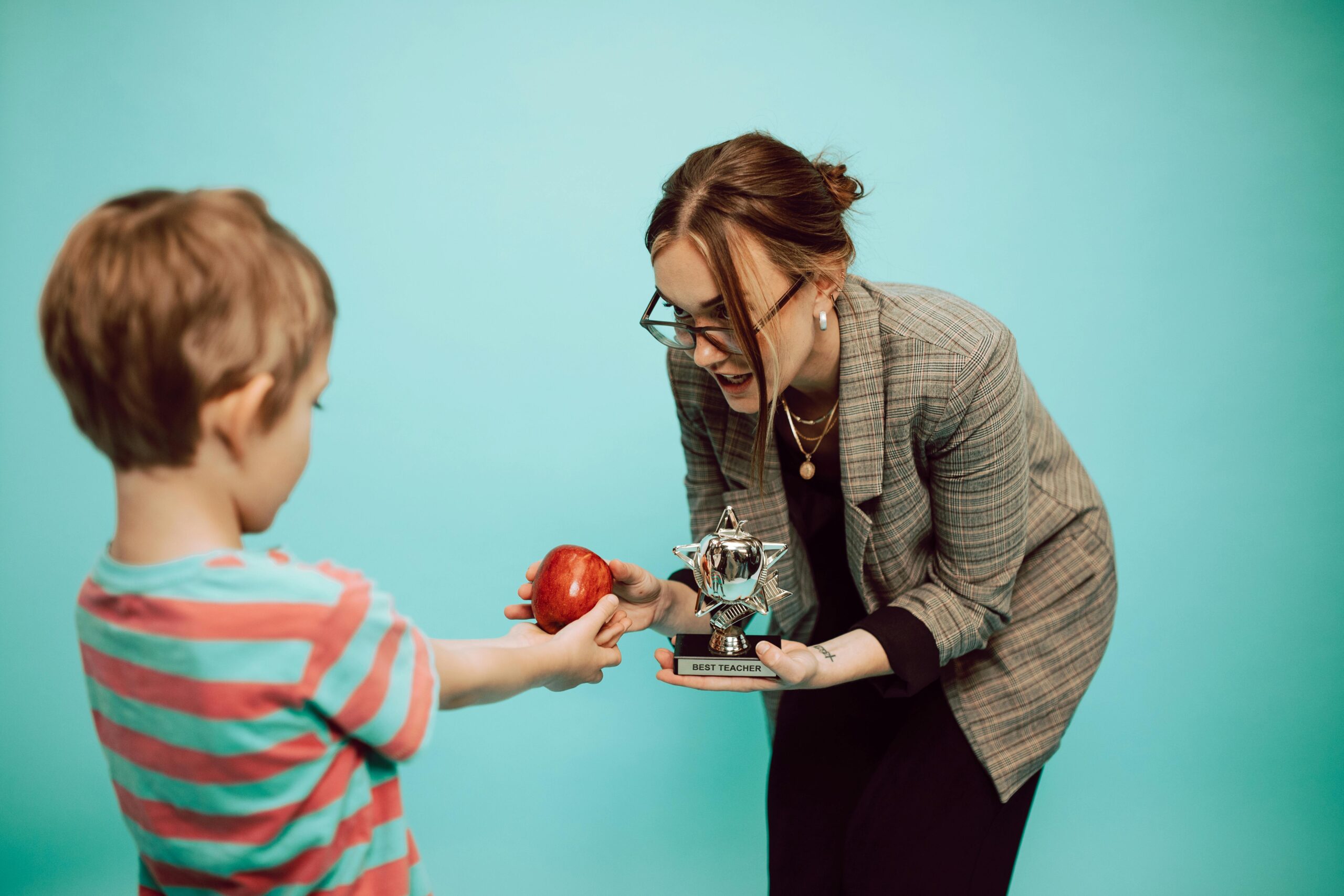 A woman giving an apple and a trophy to a boy