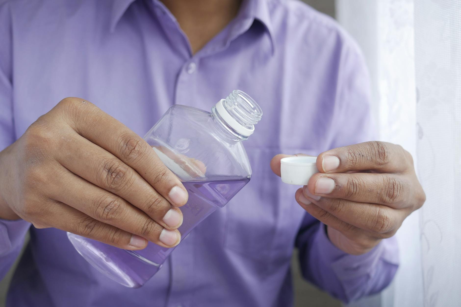 person pouring purple liquid on bottle cap