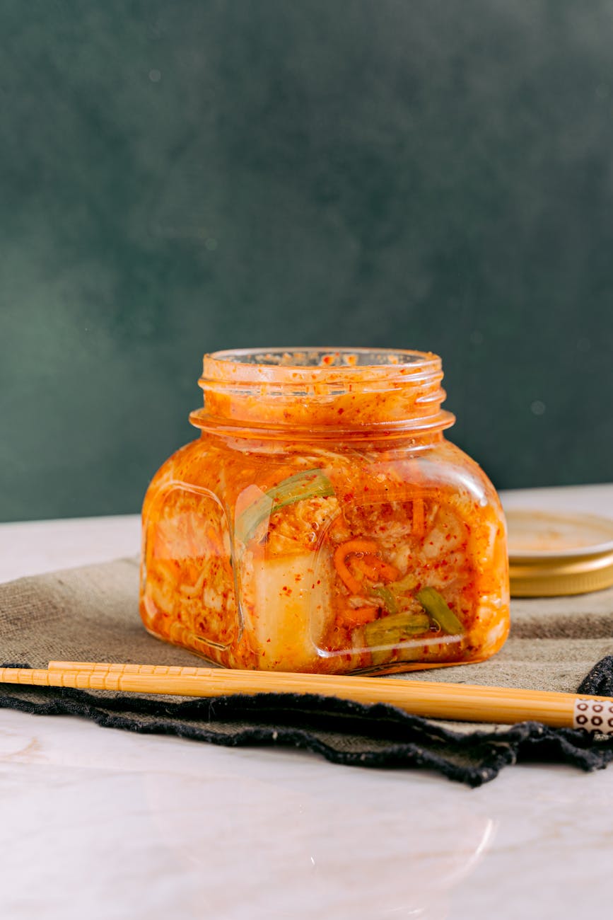 clear glass jar with kimchi beside the wooden chopsticks